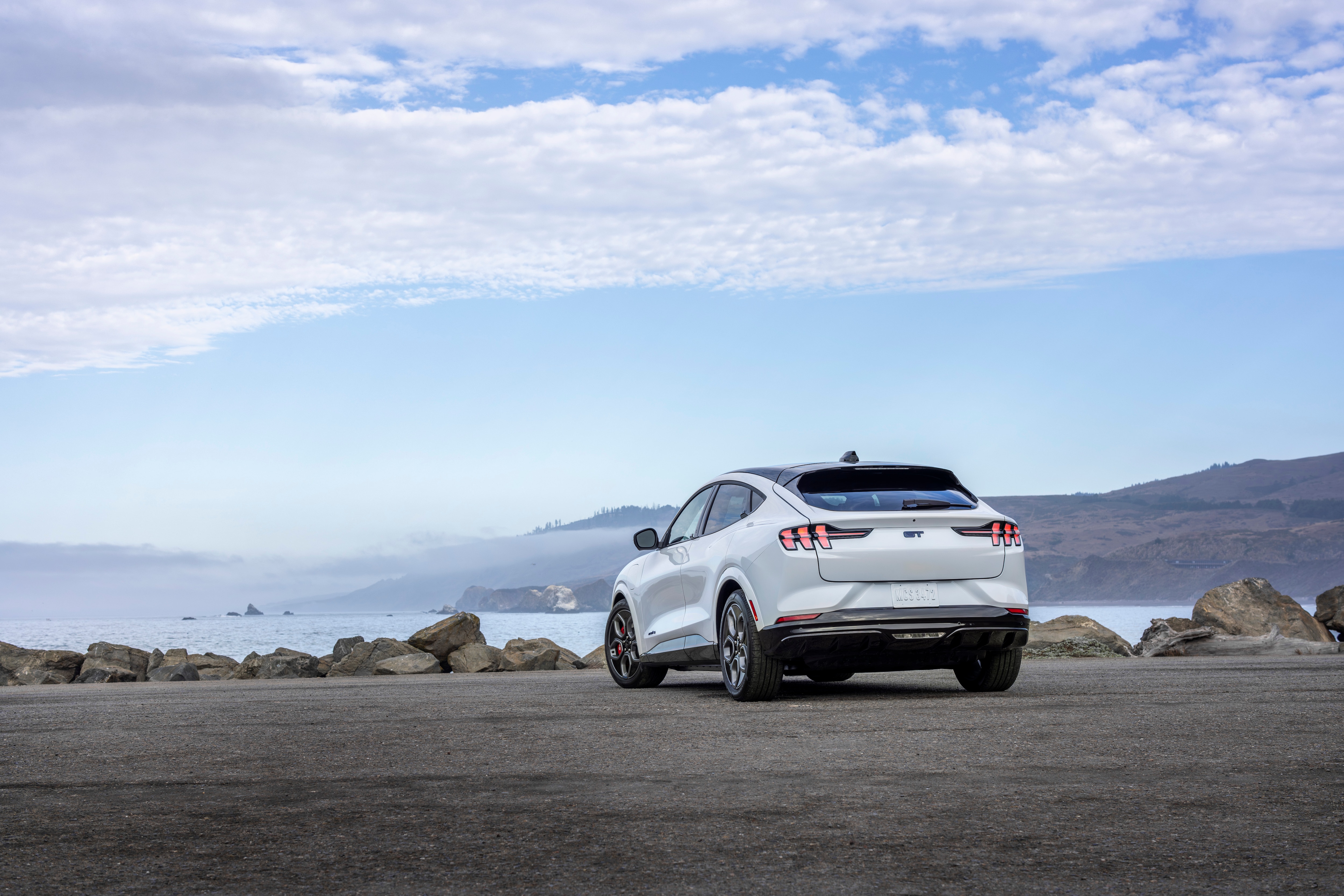 White Mustang Mach-E parked on the coastline in front of a cloudy sky. 